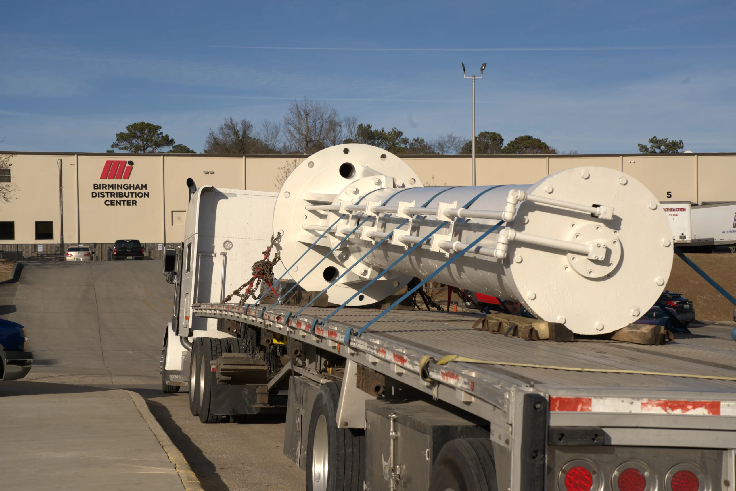 Large remanufactured hydraulic metal shaft painted white, loaded on tracker trailer at Motion's Birmingham Distribution Center with blue skies in the background