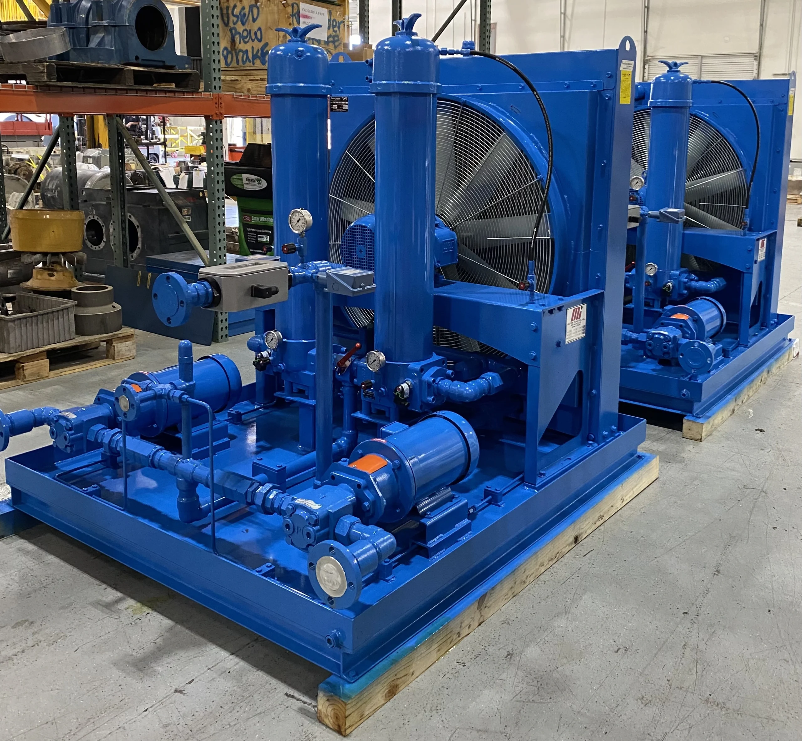 Two large custom-built hydraulic systems freshly powder coated blue sitting on pallets in remanufacture facility