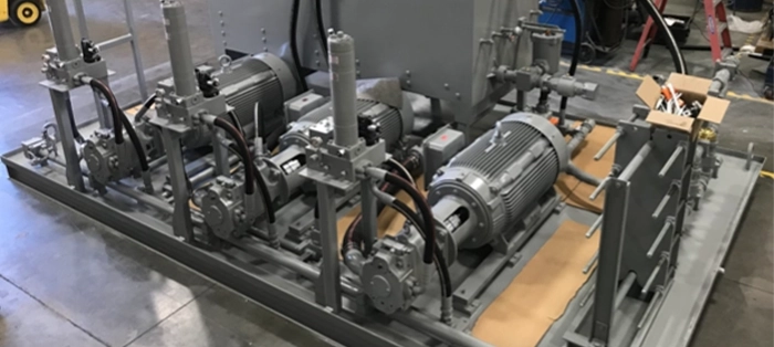 Custom built system with three large gray motors lined up to control a process pump system inside repair and services facility